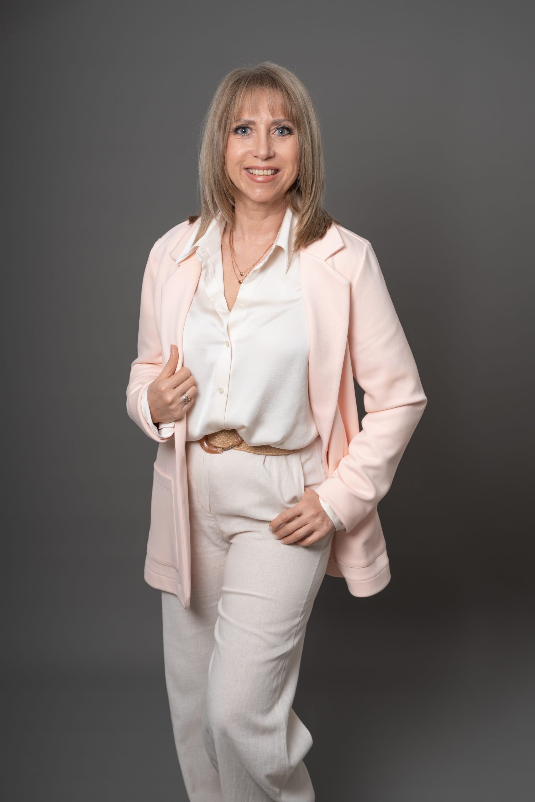 Personal Branding Fotografie Kelheim: Unternehmerin im rosafarbenen Hosenanzug, Ganzkörper vor grauem Hintergrund, Studiolicht, Anton Gil Fotografie.